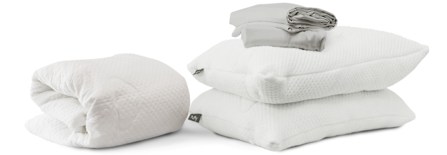 White folded mattress protector, two white pillows stacked, and a grey folded sheets set, part of the free Luxury Bedding Gifts bundle.